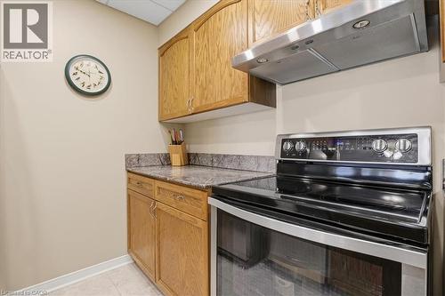 Kitchenette featuring wood cabinetry, speckled countertops, a stainless steel range hood, and a black electric range with stainless steel accents - 10 Ellen Street E Unit# 808, Kitchener, ON - Indoor Photo Showing Kitchen