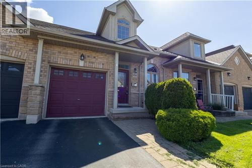 Brick facade residence featuring a burgundy garage door with upper window inserts, a covered front porch with pillar accents, a paved driveway, and mature landscaping - 4066 Medland Drive, Burlington, ON - Outdoor With Deck Patio Veranda With Facade