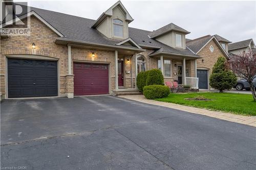 Stone and brick facade townhome featuring two distinct garage doors, dormer windows, a covered front porch, and mature front landscaping - 4066 Medland Drive, Burlington, ON - Outdoor With Facade