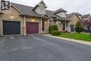 Stone and brick facade townhome featuring two distinct garage doors, dormer windows, a covered front porch, and mature front landscaping - 4066 Medland Drive, Burlington, ON  - Outdoor With Facade 