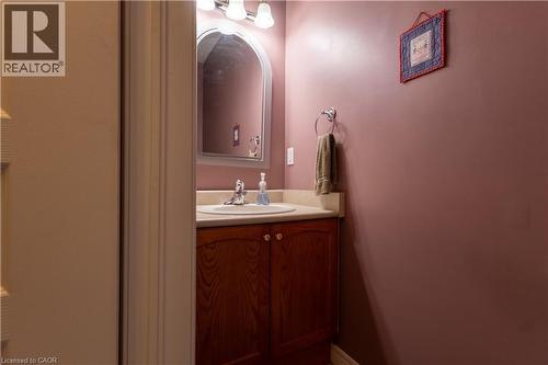 Bathroom vanity featuring a wood-finish cabinet, neutral countertop, and an arched mirror - 4066 Medland Drive, Burlington, ON - Indoor Photo Showing Bathroom