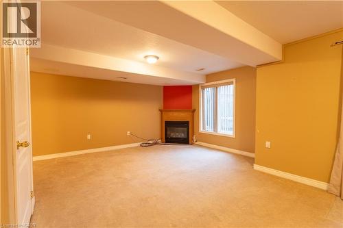 Lower level featuring a corner fireplace with a wood-finish mantel, carpet flooring, and a large window with blinds - 4066 Medland Drive, Burlington, ON - Indoor With Fireplace