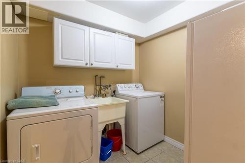 Dedicated laundry area featuring white upper cabinetry, a utility sink with dual faucets, and tiled flooring - 4066 Medland Drive, Burlington, ON - Indoor Photo Showing Laundry Room