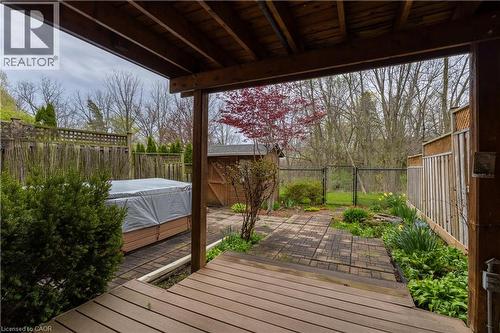 Covered wood-finish patio deck opening to a paved stone patio, mature landscaping, and a fenced perimeter - 4066 Medland Drive, Burlington, ON - Outdoor With Deck Patio Veranda