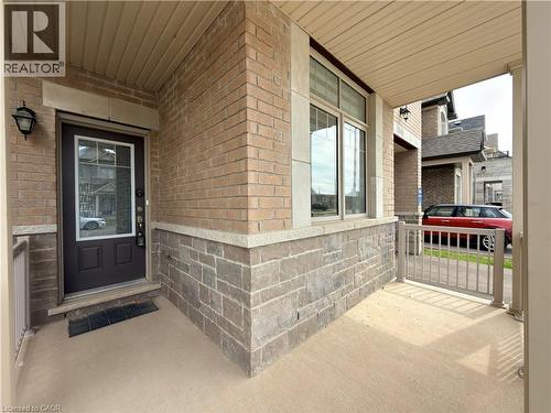 Covered front porch featuring a brick and stone facade, a dark paneled entry door with decorative glass, and a large window with stone trim - 3948 Thomas Alton Boulevard, Burlington, ON - Outdoor With Exterior