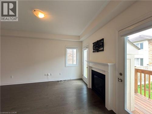 Living space featuring dark wood-finish flooring, a white mantel fireplace, and a glass-paneled door leading to an outdoor deck - 3948 Thomas Alton Boulevard, Burlington, ON - Indoor With Fireplace