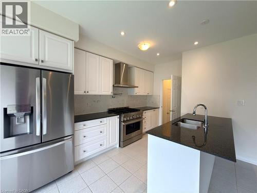 Kitchen featuring white cabinetry, dark countertops, a stainless steel French door refrigerator, a stainless steel range with an overhead vent hood, and a kitchen island with an undermount sink and ch - 3948 Thomas Alton Boulevard, Burlington, ON - Indoor Photo Showing Kitchen With Stainless Steel Kitchen With Double Sink