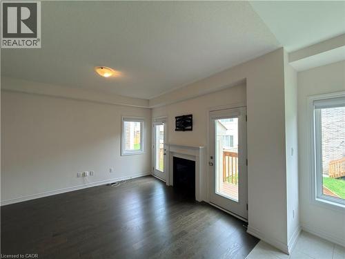 Spacious room featuring dark wood-finish flooring, white trim, a built-in fireplace with white mantel, and multiple windows - 3948 Thomas Alton Boulevard, Burlington, ON - Indoor With Fireplace