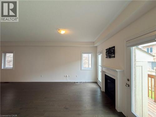 Spacious interior featuring dark wood-finish flooring, a white mantelpiece with an integrated fireplace, and multiple windows providing natural light - 3948 Thomas Alton Boulevard, Burlington, ON - Indoor With Fireplace