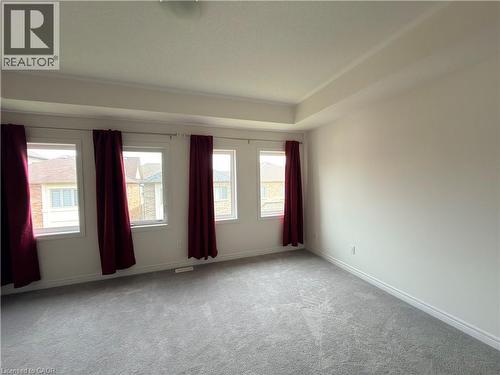 Spacious room featuring four windows with red drapes, a tray ceiling, light gray carpet, and white baseboards - 3948 Thomas Alton Boulevard, Burlington, ON - Indoor Photo Showing Other Room