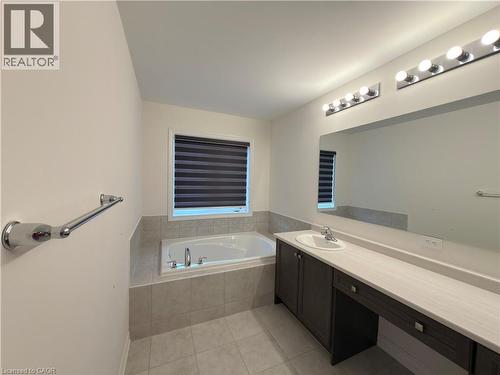 Bathroom featuring an integrated soaking tub with tiled surround, a window with horizontal blinds, a vanity with an undermount sink and extended countertop, and a large wall-mounted mirror with overhe - 3948 Thomas Alton Boulevard, Burlington, ON - Indoor Photo Showing Bathroom
