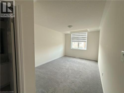Neutral-toned room featuring a window with horizontal blinds, grey carpet flooring, white baseboards, and a flush-mount ceiling light - 3948 Thomas Alton Boulevard, Burlington, ON - Indoor Photo Showing Other Room