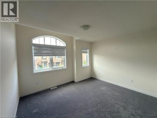 Bright interior room featuring a large arched window, a secondary rectangular window, neutral wall paint, dark carpet flooring, and a flush-mount ceiling light - 3948 Thomas Alton Boulevard, Burlington, ON - Indoor Photo Showing Other Room