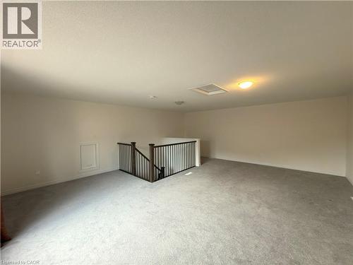 Expansive carpeted loft space featuring light neutral walls and a dark wood-finish handrail with black metal spindles - 3948 Thomas Alton Boulevard, Burlington, ON - Indoor Photo Showing Other Room