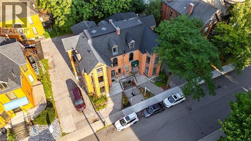 Multi-story brick building featuring a prominent gabled roofline with dormer windows, a ground-level entrance with steps, mature trees, and street-level parking - 189 Hughson Street, Hamilton, ON 