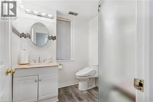 Bathroom featuring a Shower, white vanity with a granite-style countertop, a circular mirror, and a wall-mounted light fixture - 189 Hughson Street, Hamilton, ON 