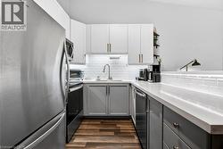 Modern kitchen featuring two-tone cabinetry, stainless steel appliances, wood-finish flooring, white subway tile backsplash, and light-toned countertops - 