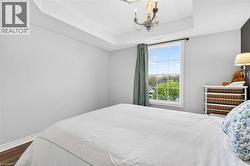 Spacious bedroom featuring wood-finish flooring, a tray ceiling, and a large window with white trim - 
