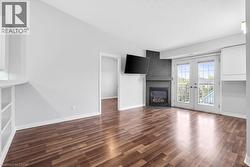 Living area featuring wood-finish flooring, a contemporary fireplace with a dark tile surround, and bright double French doors providing exterior access - 