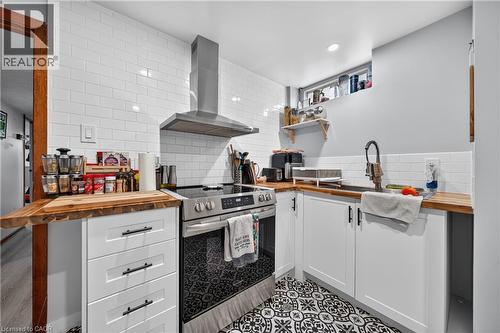 Compact kitchen featuring white subway tile backsplash, wood-finish countertops, stainless steel appliances, and patterned floor tile - 111 Kimberly Crescent, Kitchener, ON 