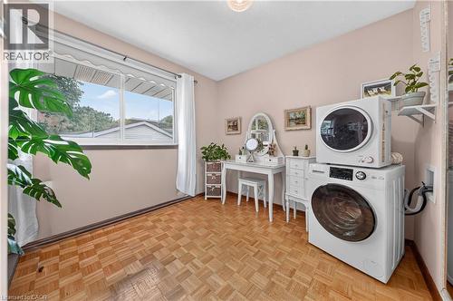 Room featuring parquet wood-finish flooring, a large window with white trim, and a built-in laundry appliance stack - 111 Kimberly Crescent, Kitchener, ON - Indoor Photo Showing Laundry Room