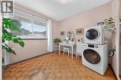 Room featuring parquet wood-finish flooring, a large window with white trim, and a built-in laundry appliance stack - 