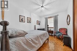 Bright bedroom featuring wood-finish parquet flooring, white walls, and a window with blinds and gray drapes - 