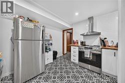 Kitchen featuring patterned flooring, white subway tile backsplash, stainless steel range with overhead vent hood, white cabinetry, and wood-finish countertops - 