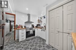 Kitchen featuring patterned floor tile, white subway tile backsplash, stainless steel range with overhead hood, and light wood-finish countertops - 