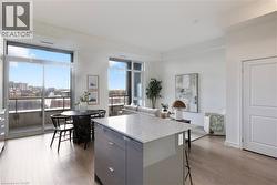 Open-concept living area featuring a kitchen island with a light-toned countertop, wood-finish flooring, floor-to-ceiling windows, and a sliding glass door leading to a balcony - 