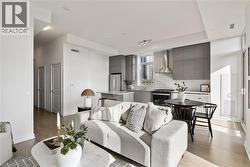 Open-concept living space featuring wood-finish flooring, recessed lighting, and a modern kitchen with grey cabinetry, stainless steel appliances, and a polished countertop island - 