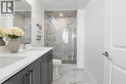 Full bathroom featuring a double vanity with integrated sinks and gray cabinetry, a glass-enclosed shower with a tiled surround, and marble-look flooring - 