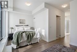 Bright bedroom featuring expansive window, wood-finish flooring, white walls, flush mount ceiling lighting, and a solid core door - 