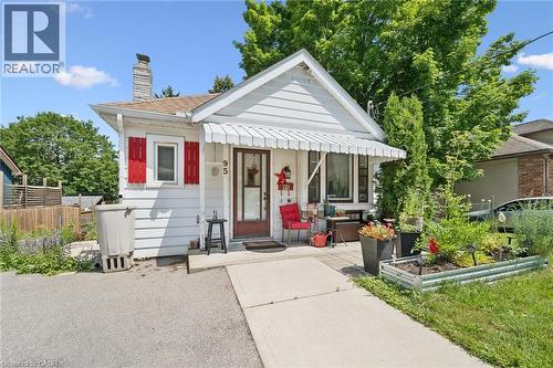 Charming bungalow featuring white siding, red window shutters, and a covered front entry with a striped awning - 95 Forest Road, Cambridge, ON - Outdoor