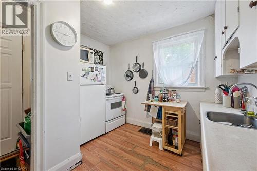 Compact kitchen featuring a window, wood-finish flooring, white cabinetry, a single basin sink, and a white refrigerator - 95 Forest Road, Cambridge, ON - Indoor Photo Showing Kitchen