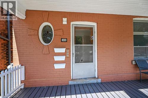 Brick facade with an oval stained-glass window, a screened entry door, and a porch featuring composite decking and a white railing - 103 Mary Street, Hamilton, ON - Outdoor With Deck Patio Veranda With Exterior