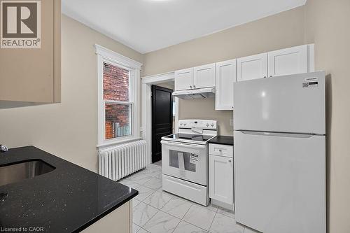 Kitchen featuring white shaker-style cabinetry, black speckled countertops, a double-basin stainless steel sink, and white appliances - 103 Mary Street, Hamilton, ON - Indoor Photo Showing Kitchen