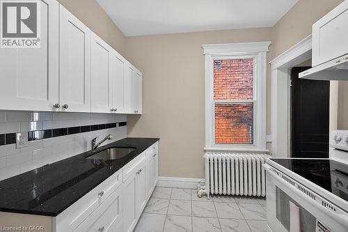 Kitchen featuring white shaker-style cabinetry, dark speckled countertops, subway tile backsplash with a black accent band, and a stainless steel sink - 103 Mary Street, Hamilton, ON - Indoor Photo Showing Kitchen
