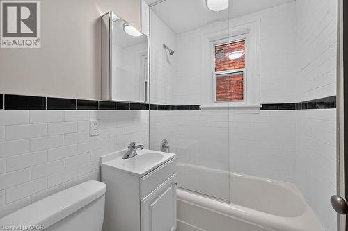 Bathroom featuring white subway tile walls with a black accent band, a white vanity with an integrated sink, a mirrored medicine cabinet, a bathtub with a clear glass shower enclosure, and a window pr - 103 Mary Street, Hamilton, ON - Indoor Photo Showing Bathroom