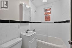Bathroom featuring white subway tile walls with a black accent band, a white vanity with an integrated sink, a mirrored medicine cabinet, a bathtub with a clear glass shower enclosure, and a window pr - 