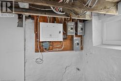 Electrical panel and subpanels mounted on a wood backing, with exposed ceiling joists and a basement window - 