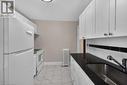 Galley kitchen featuring white cabinetry, dark speckled countertops, and a subway tile backsplash with a black accent band - 