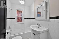White subway tile bathroom featuring a single window, built-in bathtub with shower, pedestal sink, and medicine cabinet - 
