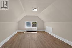 Attic space featuring wood-finish flooring, white baseboards, and a window providing natural light - 