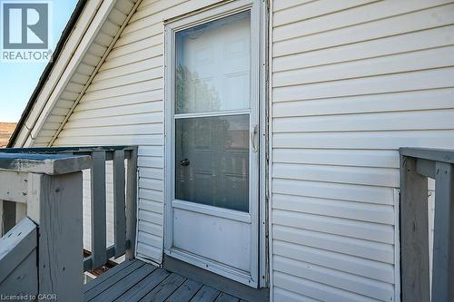 Entry door with storm door access, featuring white vinyl siding and a wooden deck railing - 103 Mary Street, Hamilton, ON - Outdoor With Exterior