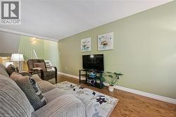 Open-concept living area featuring wood-finish flooring, light green wall paint, and white baseboards - 