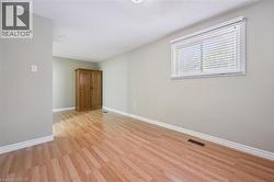 Spacious room featuring wood-finish flooring, light grey painted walls, white baseboards, and a single window with horizontal blinds - 
