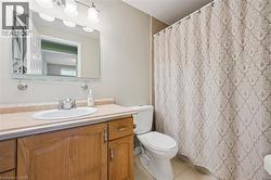 Bathroom featuring a single vanity with wood-finish cabinetry and a light-toned countertop, an oval undermount sink with a brushed nickel faucet, an overhead vanity light fixture, and a wall-mounted m - 