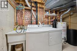 Dedicated utility space featuring laundry appliances, a utility sink, a hot water heater, exposed copper piping, and an overhead storage shelf - 