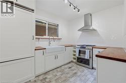 Kitchen featuring wood-finish countertops, white shaker cabinetry with dark hardware, a stainless steel range with a ventilation hood, a white farmhouse sink with a gooseneck faucet, and track lightin - 
